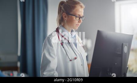 Krankenhausabteilung: Professionelle lächelnde kaukasische Ärztin trägt Labormantel und Stethoskop verwendet medizinische Geräte Computer. Patienten in Betten Stockfoto