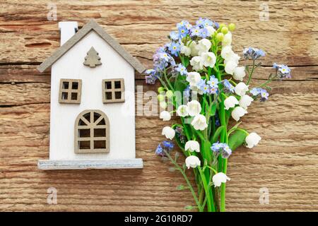 Winziges weißes Haus und Strauß von Vergissmeinnicht und Maiglöckchen Blumen auf hölzernen Hintergrund. Stockfoto