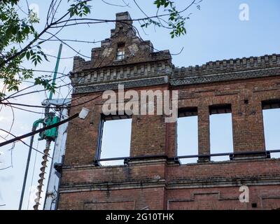 Die Außenwände aus roten Backsteinen eines alten, halb zerstörten Gebäudes mit wunderschönen Stuckverzierungen. Schlaghammer Pfahlfahrer in der Nähe für seine Rekonstruktion. Stockfoto