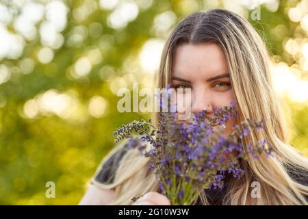 Junge glückliche Millennial Mädchen hält Strauß und Blick in die Kamera - das Modell lächelt, während sie die Blumen riecht - Outdoor Erholung Stockfoto