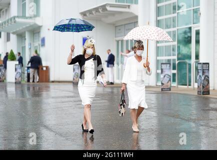 Rennfahrer schützen sich unter Regenschirmen während des Cazoo Derby Festivals auf der Epsom Racecourse am ersten Tag vor dem Regen. Bilddatum: Freitag, 4. Juni 2021. Stockfoto