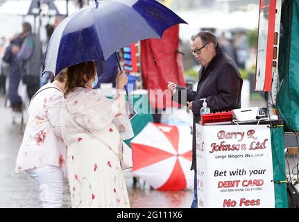 Rennfahrer schützen sich vor dem Regen unter Regenschirmen, während sie am ersten Tag des Cazoo Derby Festivals auf der Epsom Racecourse eine Wette platzieren. Bilddatum: Freitag, 4. Juni 2021. Stockfoto