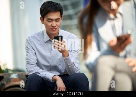 Junge asiatische Büroangestellte lesen mit Handy im Freien Stockfoto