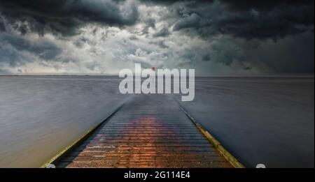 Der hölzerne Steg in Lytham in Lancashire, Großbritannien, erstreckt sich über den Sandstrand und ins irische Meer, während die Sonne untergeht und einen dramatischen Himmel erzeugt Stockfoto