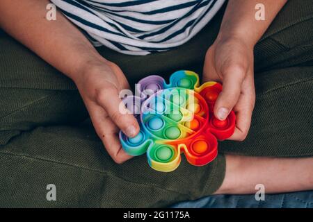 Nahaufnahme der Hände eines Jungen mit Regenbogen-Pop-it-Fidget-Spielzeug. Push Bubble Fidget Sensory Toy - waschbares und wiederverwendbares Silikon-Stressabbau-Spielzeug. Antistress Stockfoto