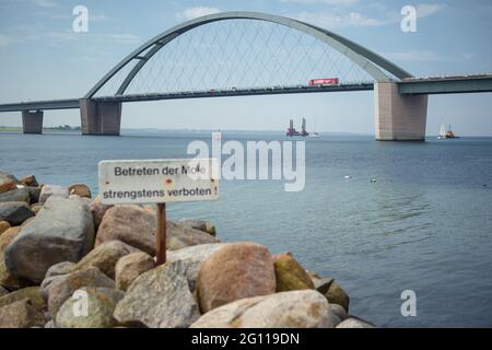 Fehmarn, Deutschland. Juni 2021. Ein LKW fährt über die Fehmarsund-Brücke, während unten während der Probebohrungen im Fehmarsund ein Bohrgerät zu sehen ist. Die Bohrungen dienen der Planung des Baus des Fehmarsundtunnels zwischen dem Schleswig-holsteinischen Festland und der Insel Fehmarn. Quelle: Gregor Fischer/dpa/Alamy Live News Stockfoto