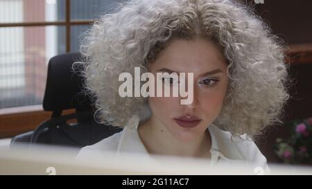 Lockiges weißes Haar Frau, die zu Hause am Computer arbeitet. Konzept für die Arbeit zu Hause. Stockfoto
