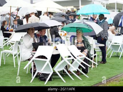 Rennfahrer schützen sich unter Regenschirmen während des Cazoo Derby Festivals auf der Epsom Racecourse am ersten Tag vor dem Regen. Bilddatum: Freitag, 4. Juni 2021. Stockfoto