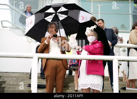 Rennfahrer schützen sich unter Regenschirmen während des Cazoo Derby Festivals auf der Epsom Racecourse am ersten Tag vor dem Regen. Bilddatum: Freitag, 4. Juni 2021. Stockfoto