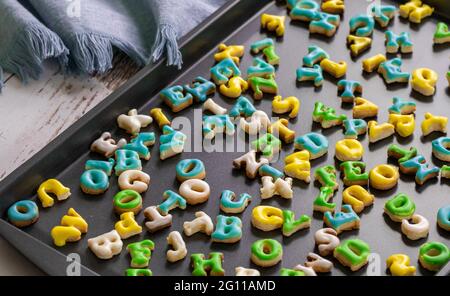 Dunkle Kochplatte voller frisch zubereiteter Kekse mit grün-blauweißer und gelber Glasur auf natürlichem Licht Stockfoto