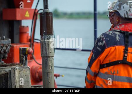 Fehmarn, Deutschland. Juni 2021. Arbeiter auf einem Bohrgerät beobachten, wie der Pfahlkernliner mit der ungestörten Bodenprobe während der Testbohrungen im Fehmarmsund ansteigt. Die Bohrungen dienen der Planung des Baus des Fehmarsundtunnels zwischen dem Schleswig-holsteinischen Festland und der Insel Fehmarn. Quelle: Gregor Fischer/dpa/Alamy Live News Stockfoto