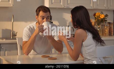 Bärtiger Mann, der Kaffee trinkt und verschwommene Freundin ansieht Stockfoto
