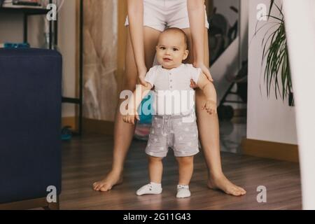 Erste Schritte des Jungen. Kleines Kind lernt, wie man geht. Mutter hilft ihrem Sohn zu gehen Stockfoto