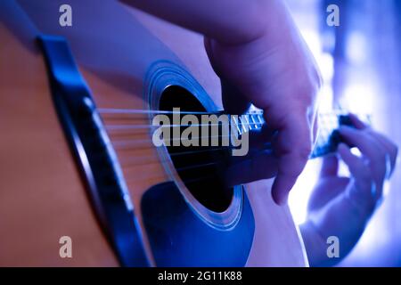 Männliche Hände spielen Finger Stil auf einer Western Dreadnought Gitarre in blauem Neonlicht Stockfoto