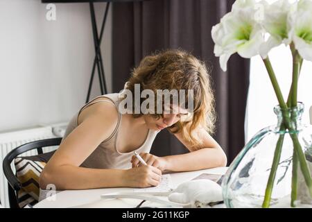 Junges Mädchen macht Hausaufgaben am weißen Tisch. Home Bildung und Homeschooling Stockfoto