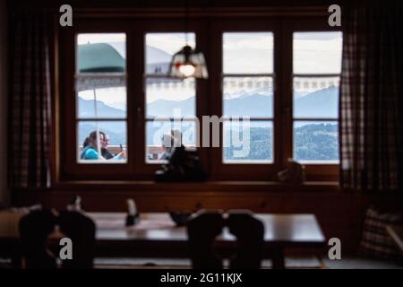 Mittenwald, Deutschland. Juni 2021. Bergsteigerinnen werden durch das Fenster des Speisesaals auf der Terrasse der Mittenwalder Hütte vor dem Panorama der Bayerischen Alpen gesehen. Die Schutzhütte nordwestlich unterhalb der westlichen Karwendelspitze auf 1518 Metern Seehöhe ist eine Alpenvereinshütte der Sektion Mittenwald des Deutschen Alpenvereins (DAV). (To dpa-Korr 'Strenge Corona-Regeln: Alpenverein fürchtet schwierige Hüttensaison' von 04.06.2021) Quelle: Matthias Balk/dpa/Alamy Live News Stockfoto