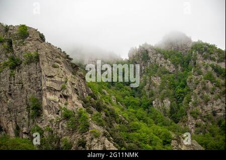 Zerklüftete, felsige Berggipfel, mit einigen Baumbeeten und tief liegenden Wolken, die die Gipfel bedecken Stockfoto