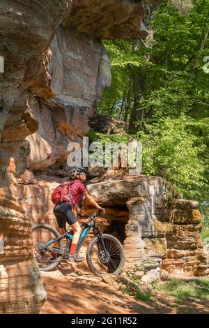 Eine nette Frau, die auf einem Felspfad im Pfaelzerwald nahe der Stadt Pirmasens in Rheinland-Pfalz mit ihrem elektrischen Mountainbike unterwegs ist Stockfoto