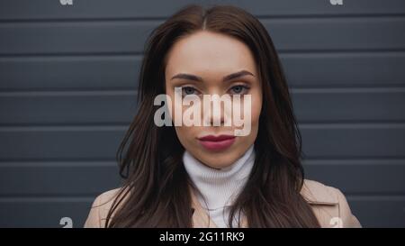 Selbstbewusste Erwachsene Frau, die die Kamera auf texturiertem grauem Hintergrund anschaut Stockfoto