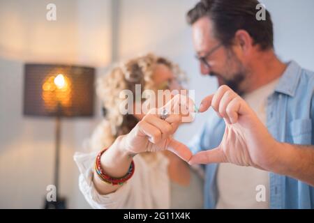 Glückliches erwachsenes Paar in der Liebe tun Herzzeichen mit Händen - Beziehung Menschen genießen zu Hause zusammen - Konzept des Menschen Und Frau verheiratet und froh für neue AP Stockfoto