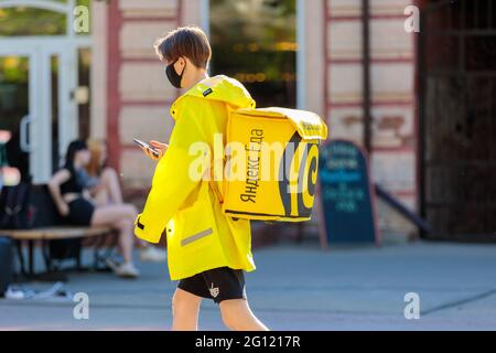 Ein Student in einer gelben Jacke und einem Rucksack liefert Essen, schaut auf das Telefon. Tscheljabinsk, Russland, 15. Mai 2021 Stockfoto