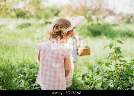 Ostereiersuche. Eine Gruppe von Kindern mit Hasenohren läuft auf der Ostereiersuche im Garten, um bunte Eier abzuholen. Ostertradition Stockfoto