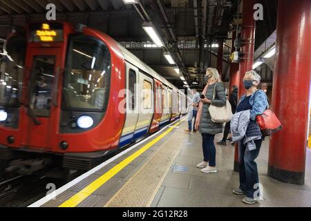 Menschen mit Masken und sozialer Distanzierung auf dem Bahnsteig, als eine U-Bahn während der COVID 19-Pandemie eintrifft, London Underground, London UK 2021 Stockfoto