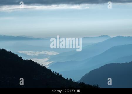 Sunrise-Szene aus Okhrey, Sikkim, Indien. Sonne geht vom Rücken des Berges auf, blauer Nebel im Mittelgrund des Bildes. Stockfoto