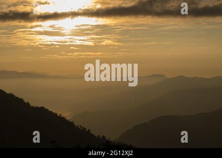 Sunrise-Szene aus Okhrey, Sikkim, Indien. Die Sonne geht vom Rücken des Berges mit orangefarbenem Glanz auf. Nebel im Bildmitte. Stockfoto