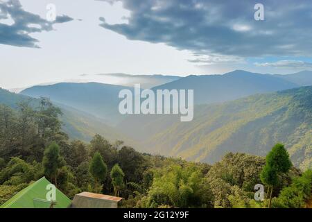 Grünes Tal zwischen Himalaya-Berghängen mit Baumlinien im Vordergrund, aufgenommen mit Morgennebel in Sikkim, Indien. Stockfoto