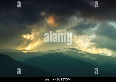 Licht, das durch das Wolkenfenster von untergehenden Sonnenstrahlen über den Gipfeln des Himalaya-Gebirges kommt. Dramatische Wolkenbildung mit Sonnenuntergangsfarben über Indian Mounta Stockfoto