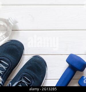Sport-Outfit auf dem weißen Holzhintergrund, Draufsicht, Kopierraum. Blaue Turnschuhe, blaue Kurzhanteln und weiße Schuppen. Modell. Stockfoto