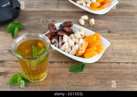 Tablett mit getrockneten Früchten und Teeglas mit Minzblättern auf Holzboden. Speicherplatz kopieren. Stockfoto