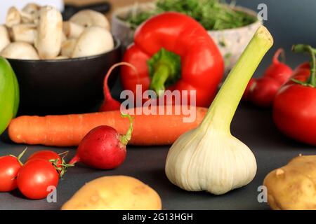 Knoblauch mit anderem Gemüse auf schwarzem Hintergrund, Paprika, Karotten, Radieschen, Pilzen, Tomaten, Kartoffeln Stockfoto