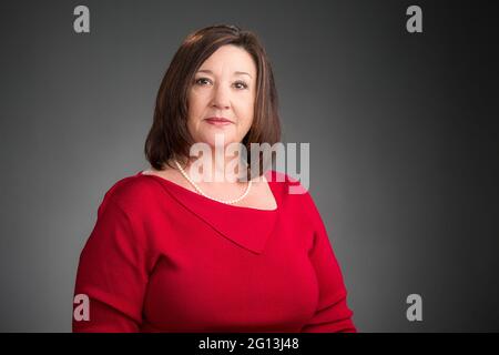 Eine leitende Frau in einem roten Pullover in einem ernsthaften Unternehmensporträt, horizontales Format auf grauem Hintergrund. Stockfoto