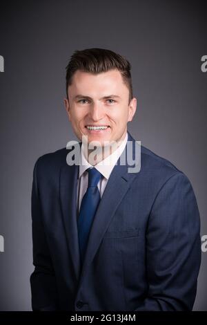Ein lächelnder Mann, ein Geschäftsführer, schaut in seinem Headshot-Portrait im Studio fröhlich auf die Kamera. Grauer Hintergrund. Stockfoto