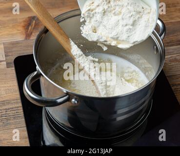 Mehl wird in einen Topf mit heißem Wasser und Butter gegossen, um eclair-Teig zu machen Stockfoto