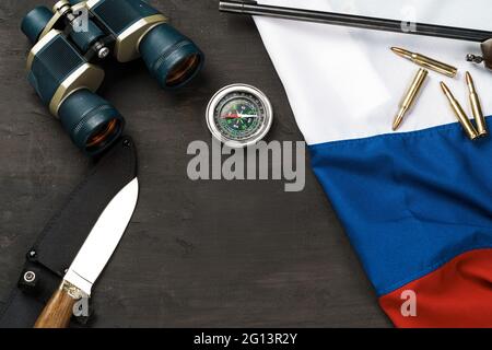 Jagdmesser, Fernglas und Patronen mit russischer Flagge auf schwarzem Hintergrund Stockfoto