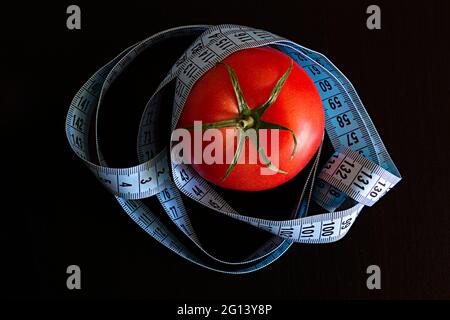 Tomate und ein blaues Meterband auf schwarzem Hintergrund, Konzept für gesunde Ernährung und Ernährung Stockfoto