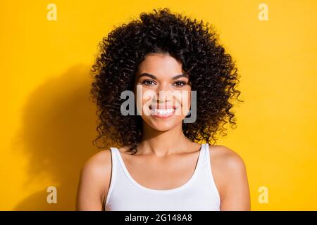 Foto von süßen hübschen jungen dunklen Haut Frau gekleidet weißen Tank-Top lächelnd isoliert gelbe Farbe Hintergrund Stockfoto