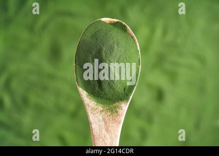 Chlorella-Algenpulver auf einem Holzlöffel über grünem Hintergrund Stockfoto