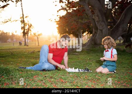 Vater und Sohn spielen Schach auf Gras im Park. Vatertag Stockfoto