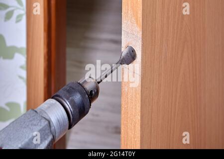 Der Tischler bohrt die Öffnung für die Verriegelung der neuen Tür mit dem flachen Bohrer. Stockfoto