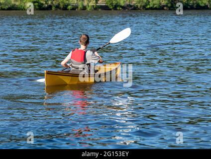 Ein junger Mann in einer Rettungsweste paddelt mit einem Kajak auf einem See in West Virginia Stockfoto