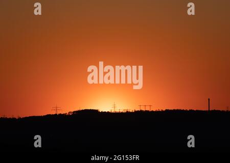 Silhouette von Hochspannungsleitungen und Pylonen vor einem schönen Sonnenuntergang - klarer und wolkenloser Himmel Stockfoto