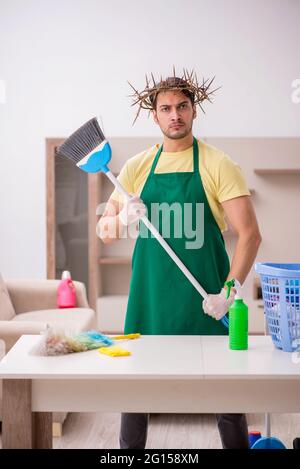 Junger männlicher Auftragnehmer, der auf dem Kopf einen stacheligen Kranz trägt und Hausarbeit leistet Stockfoto