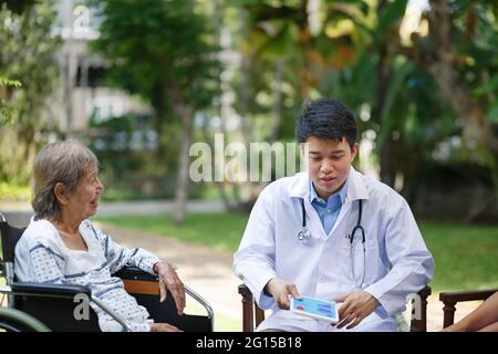 Asiatische Arzt im Gespräch mit älteren weiblichen Patienten auf Rollstuhl Stockfoto