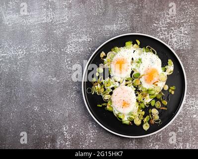 Spiegeleier mit Lauch auf einem runden Teller auf dunklem Grund. Draufsicht, flach liegend Stockfoto