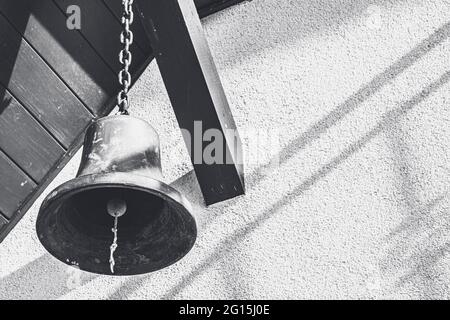 Die große, alte Schiffsglocke hängt als Dekoration an einem Holzbalken - die Glocke als Dekoration an einer Kette. Stockfoto