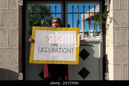 Eine Palästinenserin hält ein Plakat mit der Aufschrift „Stoppt die Besatzung“ während einer Demonstration gegen israelische Besatzung und Siedlungsaktivitäten in Scheich Jarrah, einem überwiegend palästinensischen Viertel, am 04. Juni 2021 in Jerusalem, Israel. Das palästinensische Viertel Sheikh Jarrah ist derzeit das Zentrum einer Reihe von Eigentumsstreitigkeiten zwischen Palästinensern und rechtsgerichteten jüdischen Israelis. Einige Häuser wurden nach einem Gerichtsurteil von israelischen Siedlern besetzt. Stockfoto